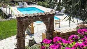 A rectangular swimming pool with a tiled deck, surrounded by a brick archway, and a wooden deck area with a bench. - Luxury villa with pool on the slopes of Etna (Nicolosi)