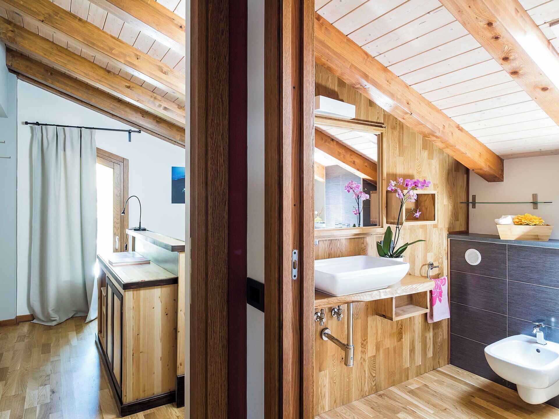 A wooden interior with a wooden ceiling, a white sink, a bidet, and a mirror.