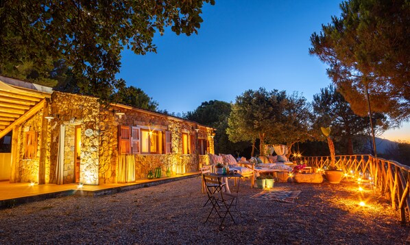 Un edificio de piedra con una terraza de madera y un espacio cubierto con cojines y una mesa.