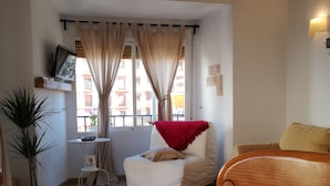 A cozy living room with a white armchair, a wooden table, and a TV on a shelf. - Apt. Santa in the old town, unsoperable views and just 3 minutes from the beach (Alicante)