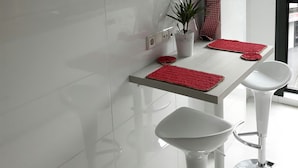 Une cuisine moderne avec des carreaux blancs, une horloge, un tableau, une plante en pot et des sets de table rouges posés sur le comptoir.