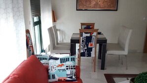 Un salon moderne avec un canapé rouge, des coussins à motifs, une table à manger avec des chaises et une grande œuvre d’art encadrée accrochée au mur.