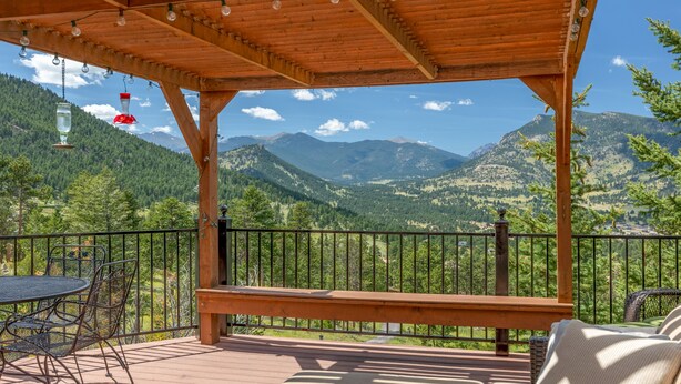A wooden deck with a table and chairs, overlooking a mountainous landscape.