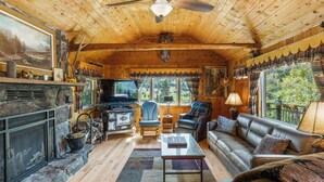 A cozy cabin interior with a stone fireplace, leather sofa, and a television.