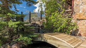 A wooden bridge over a small stream, surrounded by greenery and stone walls.