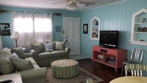 Een woonkamer met een bank, voetenbankje, tv-meubel en een plafondventilator.