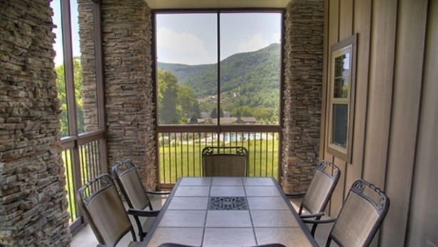 Eine überdachte Terrasse mit Steinmauer, Tisch und Stühlen sowie Blick auf eine Berglandschaft.
