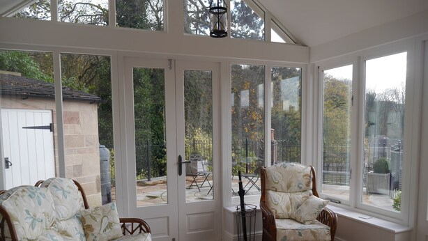A sunroom with a view of a garden, two wicker sofas, a glass coffee table, and a patterned armchair.