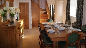 A dining area with a wooden table set for four, green upholstered chairs, and a staircase in the background.