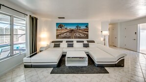 A modern hotel room with a sectional sofa, a flat-screen TV, a large window with a view of a pool, and a painting of a road on the wall. - BOATERS.HOUSE  South Florida Ranch in Cape Coral, Florida (Cape Coral)