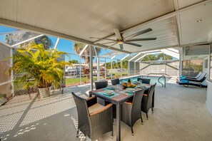 A covered outdoor area with a pool, lounge chairs, and dining table with chairs.