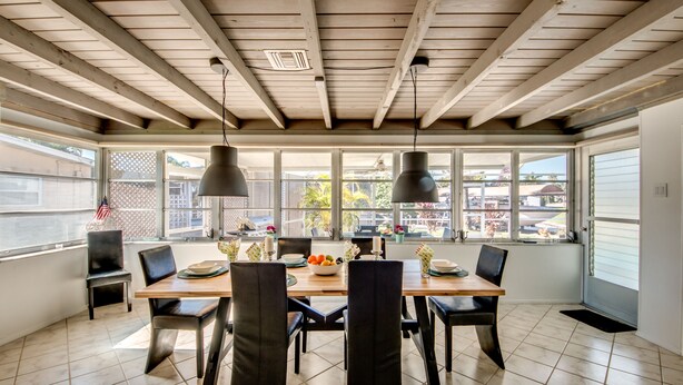 A dining area with a wooden table and chairs, large windows, and hanging pendant lights. - BOATERS.HOUSE  South Florida Ranch in Cape Coral, Florida (Cape Coral)