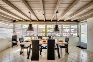 A dining area with a wooden table and chairs, large windows, and hanging pendant lights.