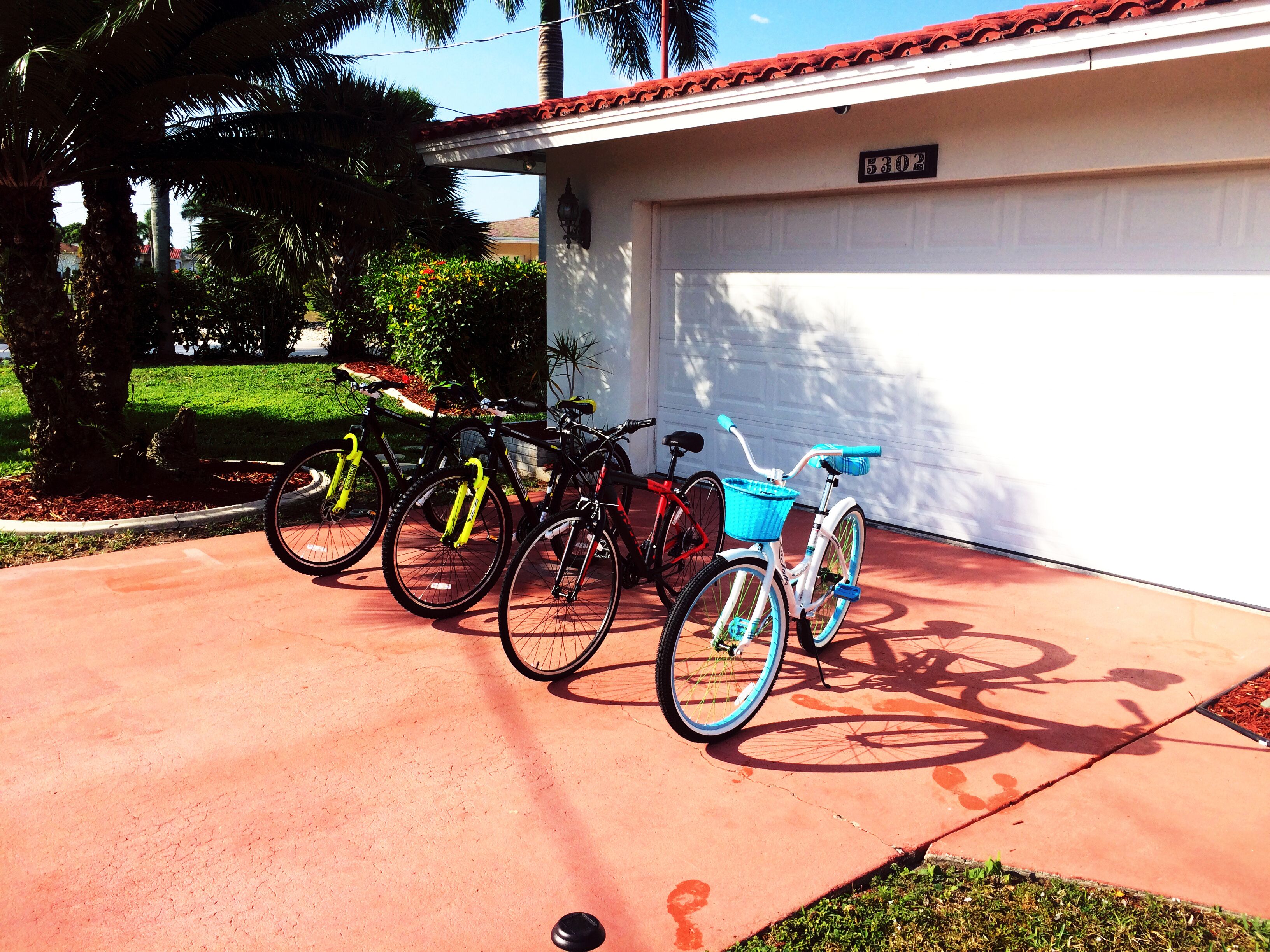 Uma garagem com porta de número 5302, uma bicicleta com cesto azul e outra bicicleta vermelha encostada na parede.