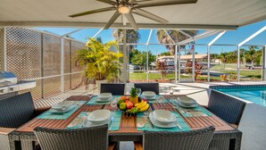An outdoor patio with a table set for dining, surrounded by wicker chairs, a ceiling fan, and a view of a swimming pool and palm trees. - BOATERS.HOUSE  South Florida Ranch in Cape Coral, Florida (Cape Coral)