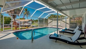 A covered outdoor swimming pool with lounge chairs and a view of palm trees. - BOATERS.HOUSE  South Florida Ranch in Cape Coral, Florida (Cape Coral)