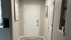 A hallway with a white door, a rug, and a small shelf with a picture. - Newly Updated, 2 King Beds, Pools, Hot Tub & Golf Course Views! Feels like home! (Branson)