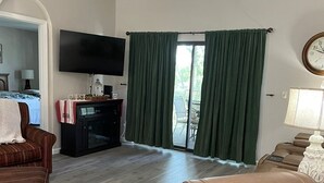A living room with a brown leather sofa, a television, and a sliding glass door with green curtains. - Newly Updated, 2 King Beds, Pools, Hot Tub & Golf Course Views! Feels like home! (Branson)