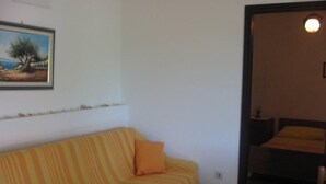 A room with a striped sofa, a painting on the wall, and a bed with a yellow pillow. - Apartment in garden 400m from the sea (Jelsa)