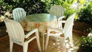 A round table with a floral tablecloth surrounded by four white plastic chairs with plaid cushions. - Apartment in garden 400m from the sea (Jelsa)
