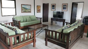 Una sala de estar con un sofá verde, una mesa de centro de madera y un televisor sobre un mueble.