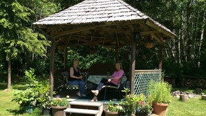 Un kiosque en bois avec un toit en tuiles, entouré de plantes en pot et d’une pelouse.