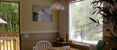 A dining area with a wooden table, white chairs, and a window with blinds.