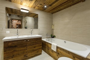 A modern bathroom with a wooden vanity, a large mirror, a bathtub, and a toilet.