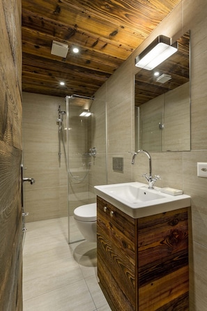 A modern bathroom with a wooden ceiling, a glass shower enclosure, a white sink, and a wooden vanity.