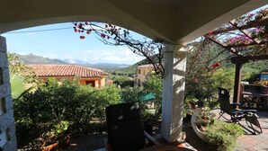 Un porche cubierto con vistas a un paisaje montañoso, una mesa de madera y una silla.
