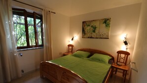 Un dormitorio con cama de madera, ropa de cama verde, una ventana con cortinas, un cuadro colgado en la pared y lámparas de noche.