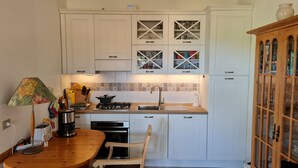Una cocina compacta con armarios blancos, una mesa de madera y un horno empotrado.