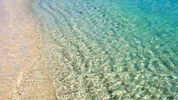 Una playa con agua turquesa cristalina, una orilla arenosa y una montaña al fondo.
