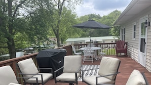 Eine überdachte Terrasse im Freien mit vier Stühlen und einem Tisch, einem Grill und einem großen Sonnenschirm.