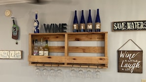 Eine Wand mit einem Weinregal, das Flaschen und Gläser beherbergt, einer Uhr sowie verschiedenen Schildern, darunter ‚WINE TIME‘ und ‚SAVE WATER‘.