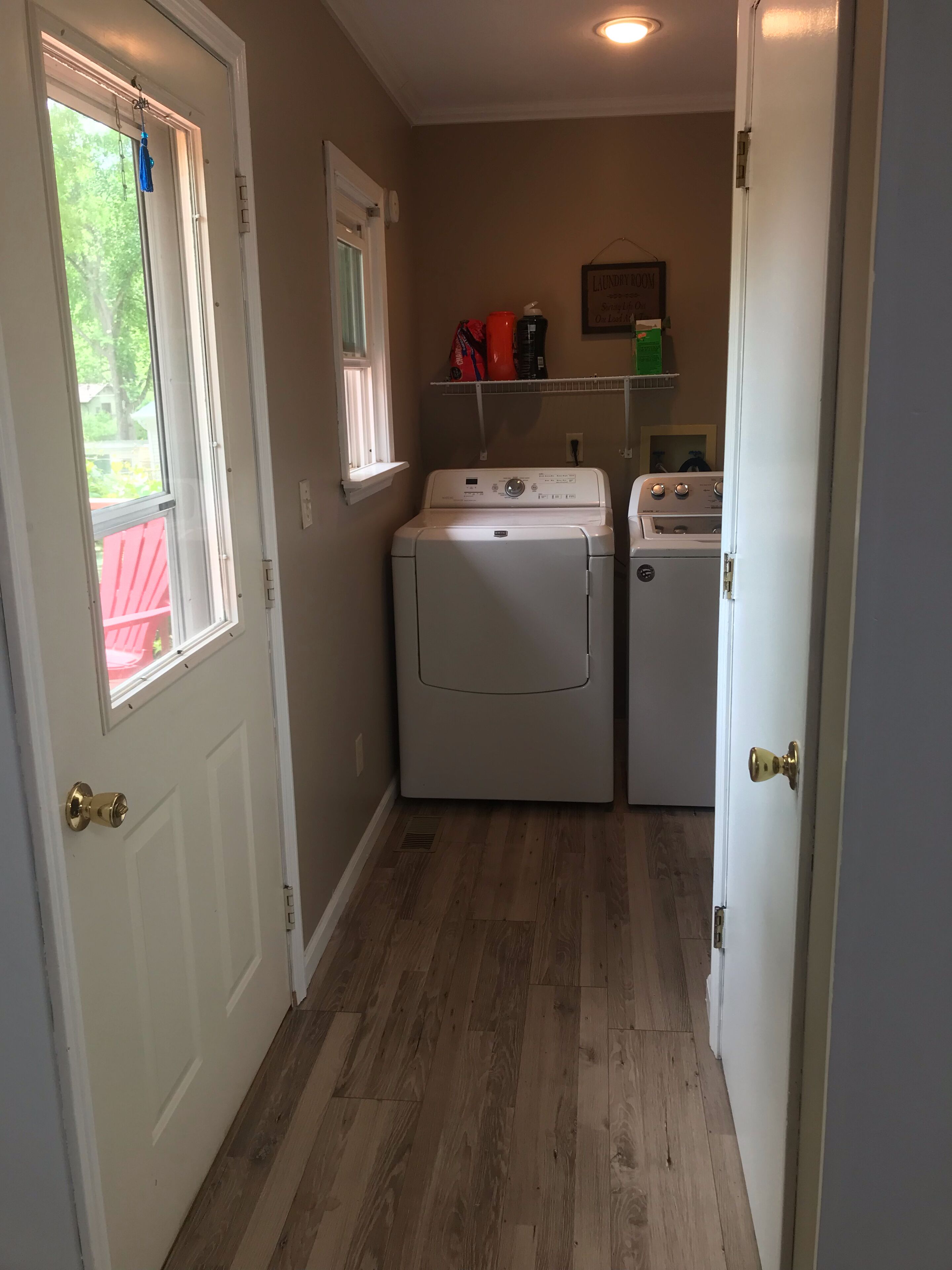Une buanderie équipée d’un lave-linge et d’un sèche-linge, avec un plancher en bois et une fenêtre donnant sur un espace verdoyant.