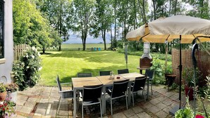 A patio with a table and chairs, a grill, and a view of a grassy field and trees.