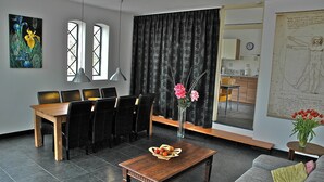A modern living room with a dining area, featuring a wooden table, black chairs, a wooden coffee table, and a vase with flowers.