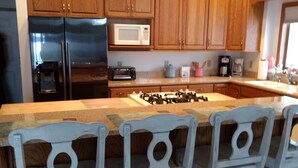 A kitchen with wooden cabinets, a stainless steel refrigerator, a microwave, a gas stove, and three white chairs with a unique design.