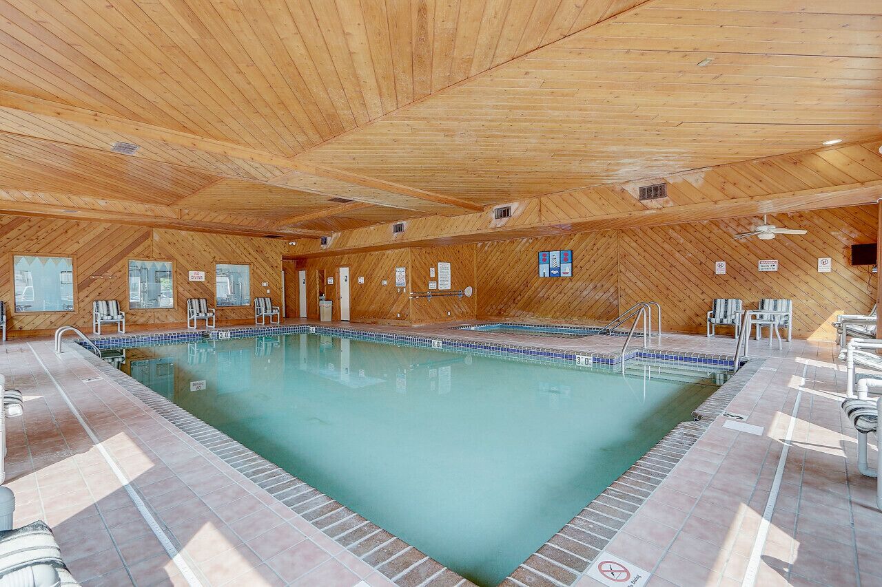 Une piscine intérieure aux murs et au plafond en bois, entourée de chaises longues.