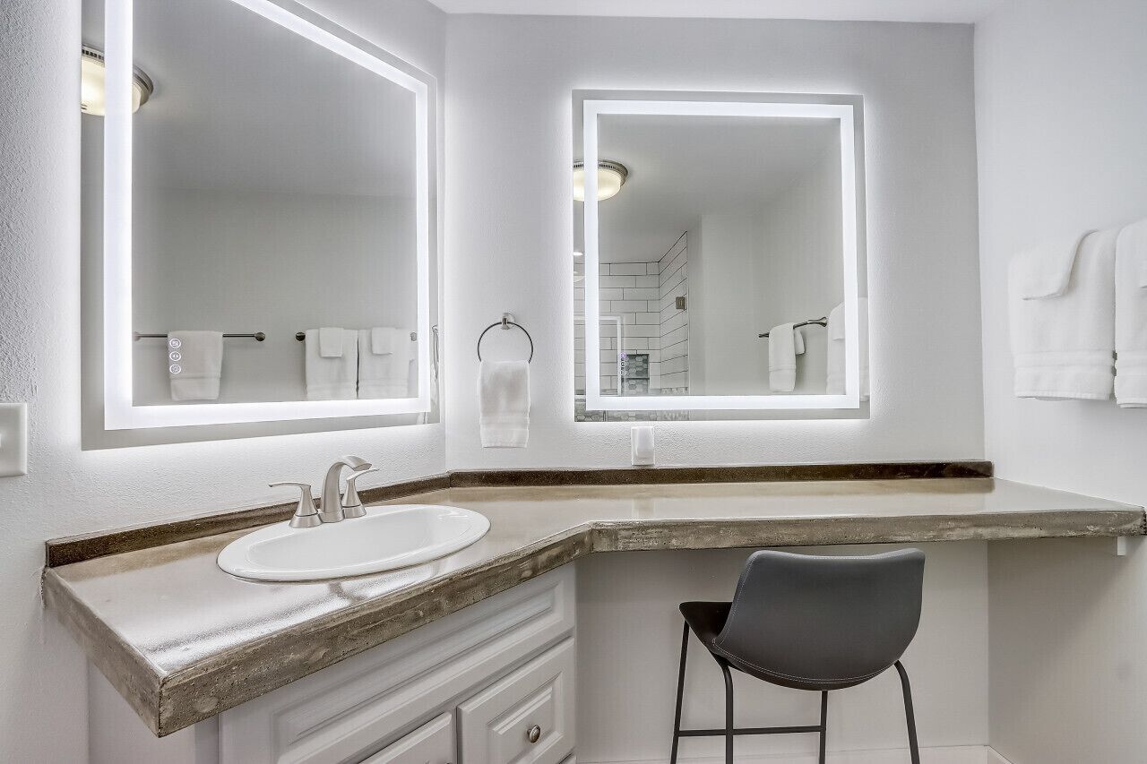A bathroom with a large mirror, a sink, and a chair.