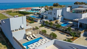 A modern hotel with multiple swimming pools, outdoor seating areas, and a view of the sea.