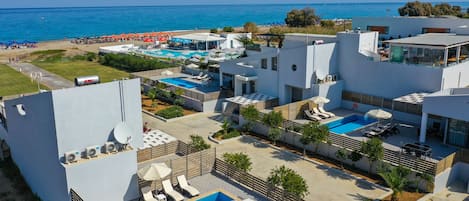 A modern hotel with multiple swimming pools, outdoor seating areas, and a view of the sea.