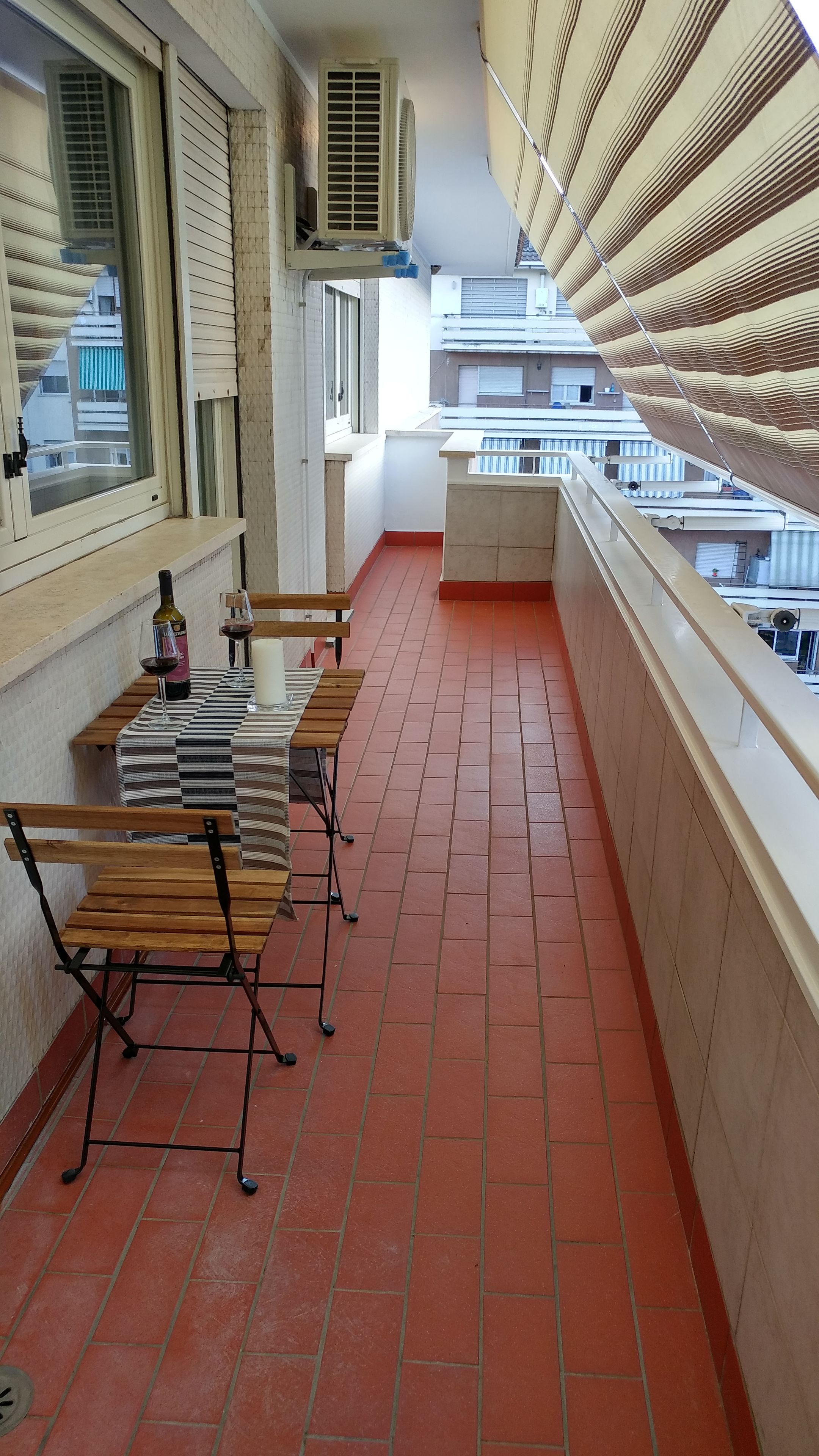 A balcony with a tiled floor, a table with chairs, and a view of buildings in the background.