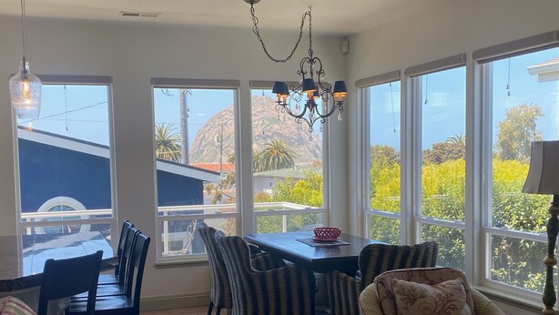 A spacious dining area with a table and chairs, large windows offering a view of the outdoors, and a chandelier hanging above. - Beautiful ocean retreat (Morro Bay)
