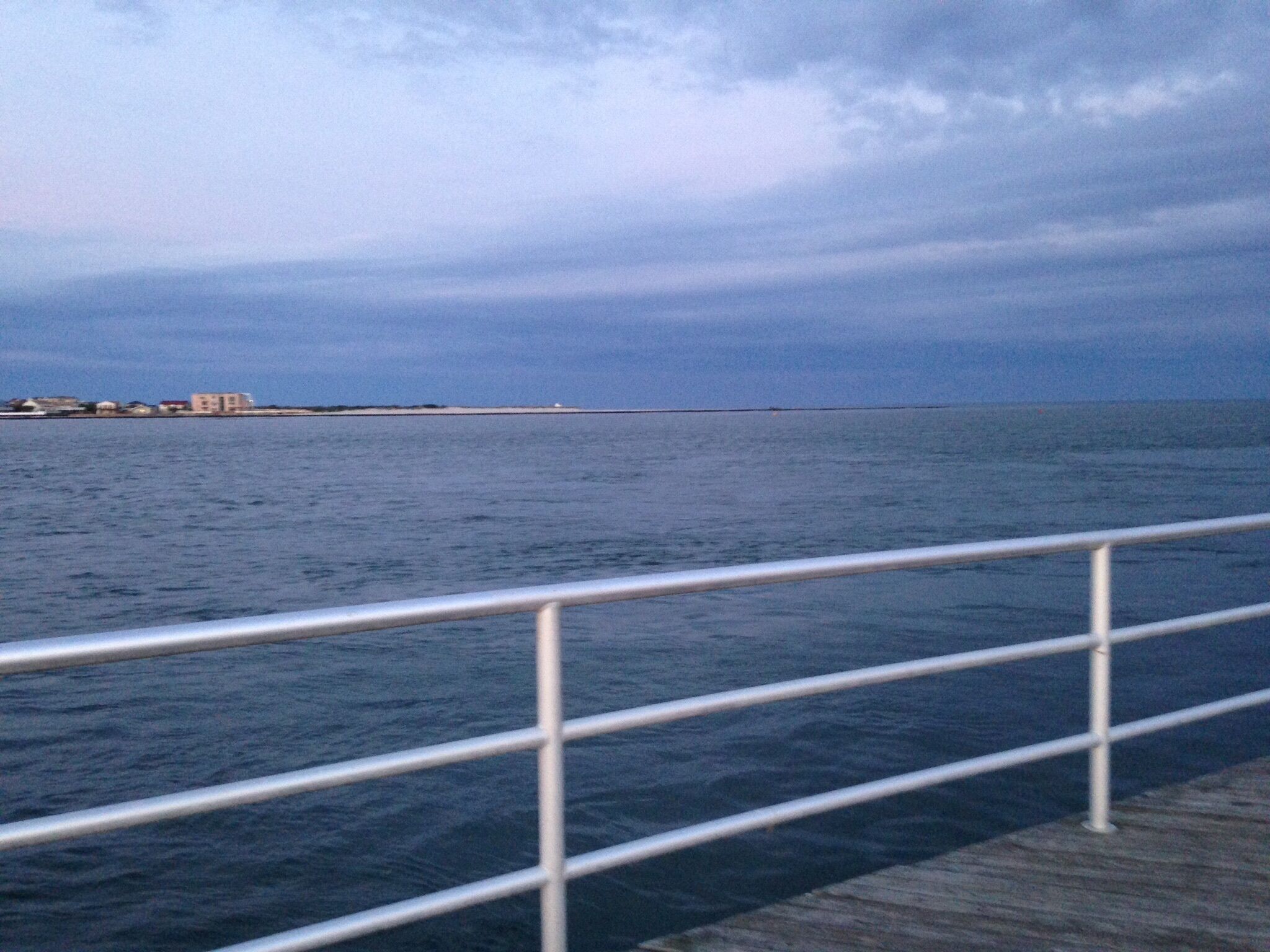 A view of a body of water with a distant shoreline and a metal railing in the foreground.
