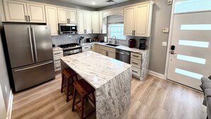 A modern kitchen with a marble island, stainless steel appliances, and light-colored cabinetry.