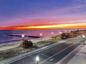 Una carretera costera con farolas y vista al océano al atardecer.