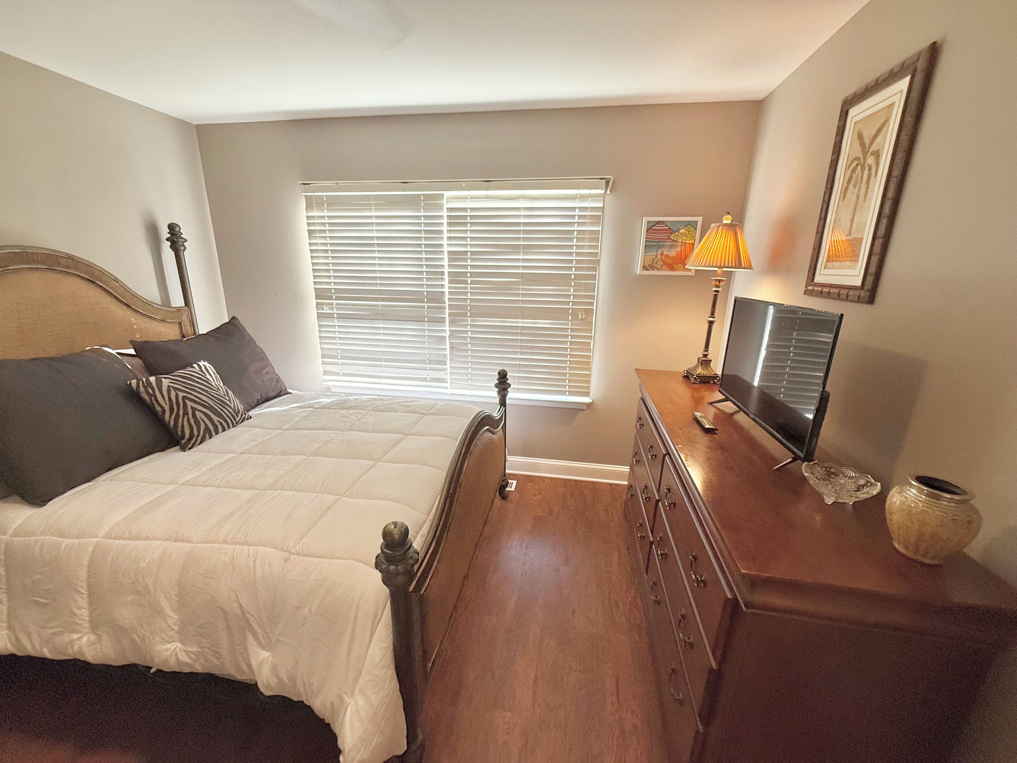 A bedroom with a bed, a dresser, a television, and a window with blinds.