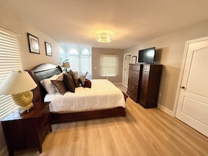 Een slaapkamer met een bed, een dressoir, een televisie en ramen.